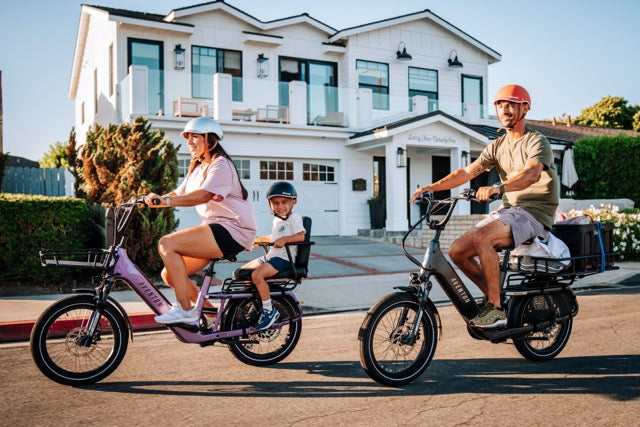 Parents riding an Aventon Abound SR cargo ebike with a captains chair in haze and stealth available at CyclErie in Erie, CO.