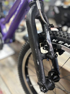 Angled view of a pre-loved Prevelo Alpha One 14" kids' bike in Power Purple, displayed on a dirt trail, featuring a lightweight frame and rugged tires for young adventurers.
