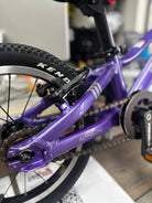 A well-maintained Prevelo Alpha One 14" kids' bike in Power Purple, standing on a paved path, with a sleek design for beginner cyclists.
