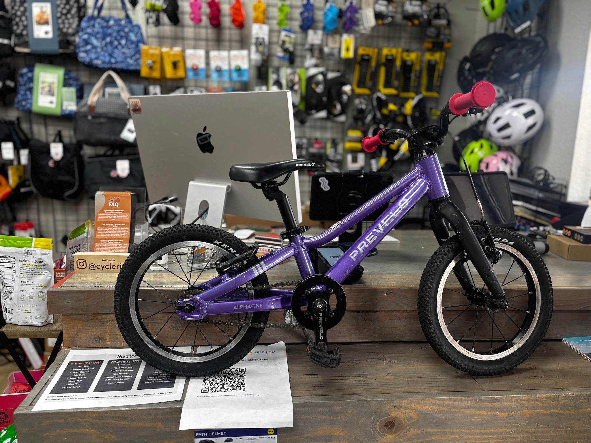 Side view of a used Prevelo Alpha One 14" bike in vibrant Power Purple, showing minor wear on the frame, positioned against a park backdrop.
