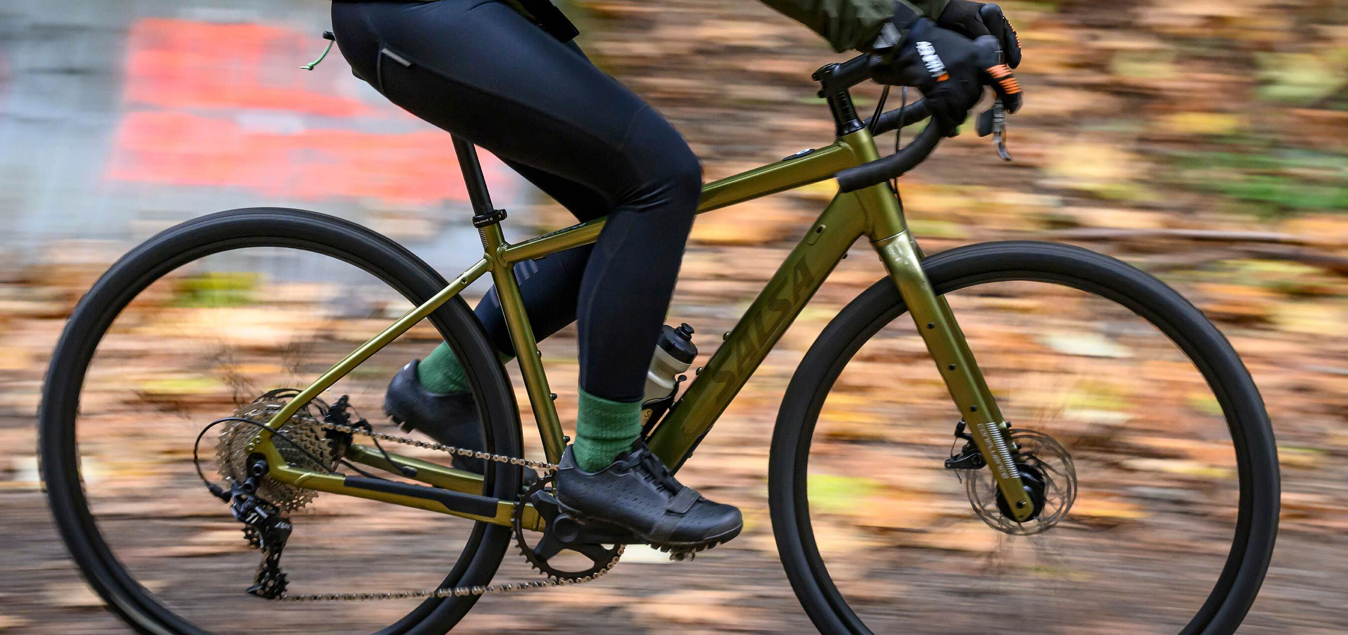 Image of a person riding quickly on an electric gravel bicycle with autumn leaves in the background